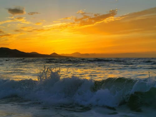 Golden sunset over waves at Arguineguín beach with mountains silhouetted on horizon
