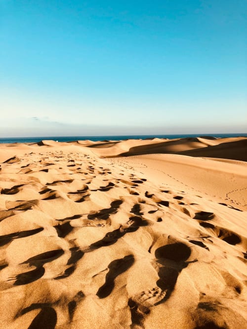 Golden sand dunes meeting turquoise ocean under blue sky in Arguineguín, coastal landscape view