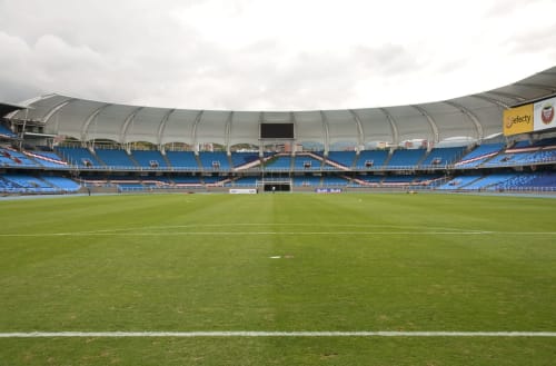 Moderno estadio con asientos azules, campo verde y techo curvo distintivo en Cali, Colombia