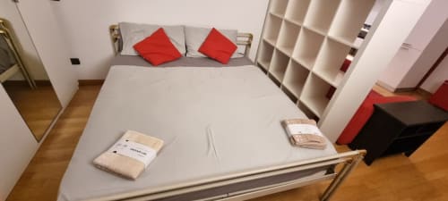 Modernes Schlafzimmer in der Novara Home Wohnung in Milano mit Bett, roten Kissen, weißen Regalen und Holzfußboden