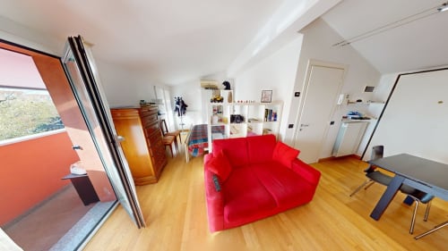 Rotes Sofa in hellem Wohnzimmer eines Mailänder Apartments mit Holzböden, moderner Küche und Balkon mit Stadtblick