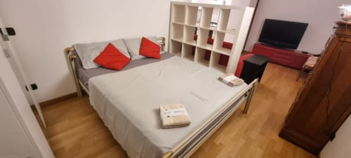 Modernes Schlafzimmer im Come a Casa Tua Milano Apartment mit weißem Bett, roten Kissen, weißen Regalen, TV und Holzboden