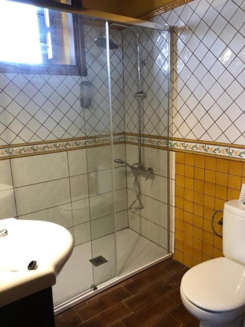 Modern bathroom with glass shower enclosure, white tiles, yellow accent tiles, and dual toilets at Casonas de Marengo cottage