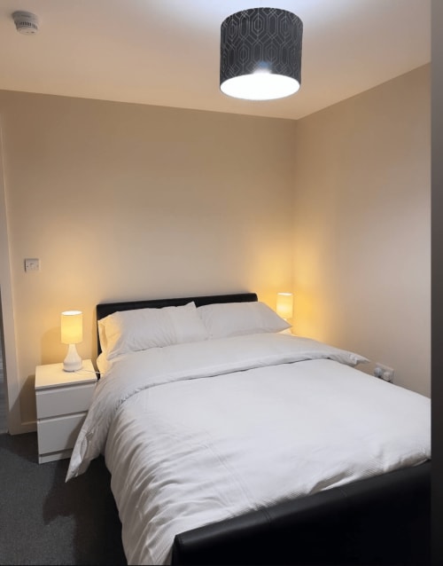Modern bedroom at Cila Property Manchester with queen bed, black headboard, white bedding, geometric ceiling light, and