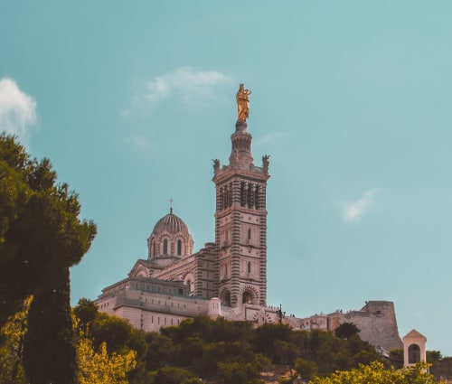 La Basilique Notre-Dame de la Garde surplombe Marseille avec sa statue dorée et son campanile de pierre sous un ciel bleu