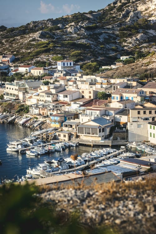 Village de pêcheurs côtier à Marseille avec maisons blanches, bateaux au port et collines calcaires rocheuses