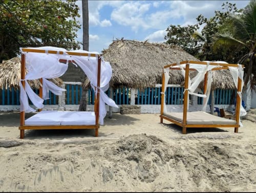 Dos camas dosel de madera con cortinas blancas en playa arenosa del hotel Olamar Living en Santiago de Tolú, Colombia