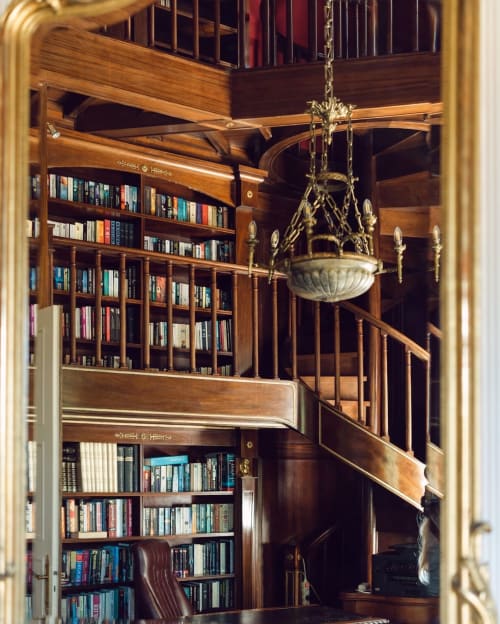 Élégante bibliothèque avec escalier en spirale en bois, étagères du sol au plafond et lustre en laiton au Domaine de Bize