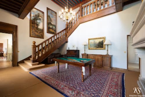 Elegante sala de billar con escalera de madera, muebles de época y obras enmarcadas en el Domaine de Bize en Mirepoix