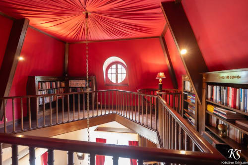 Salon bibliothèque mezzanine rouge avec baie vitrée circulaire au Domaine de Bize Mirepoix en Ariège