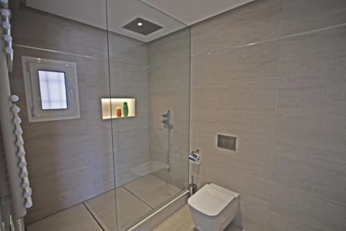 Modern bathroom in Marbella penthouse with glass shower enclosure, white toilet, and tiled walls