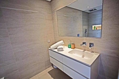 Modern bathroom with double sink vanity, large mirror, and beige tile walls in Marbella penthouse apartment