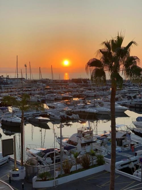 Sunset over Puerto Banús marina with sailboats and palm trees, Marbella sea view apartment balcony
