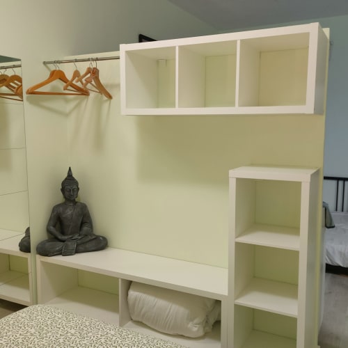 Unidad de estanterías en dormitorio con estatua de Buda, perchas de madera y almacenamiento en el apartamento Megaleon de Segovia