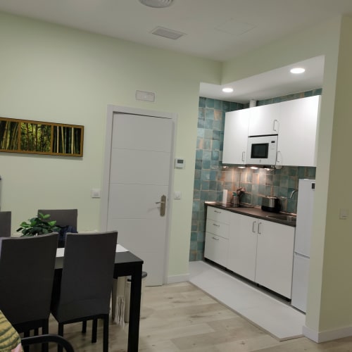 Cocina y comedor modernos en el apartamento Megaleon, Segovia con muebles blancos y azulejo verde azulado