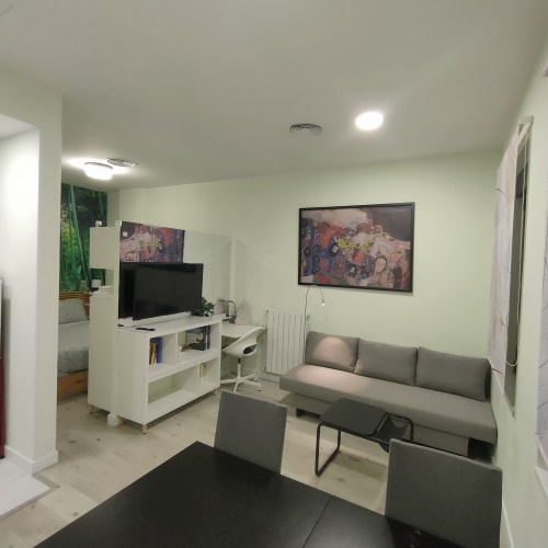 Salón moderno de apartamento en Megaleon Segovia con sofá gris, TV, escritorio y luces de techo brillantes