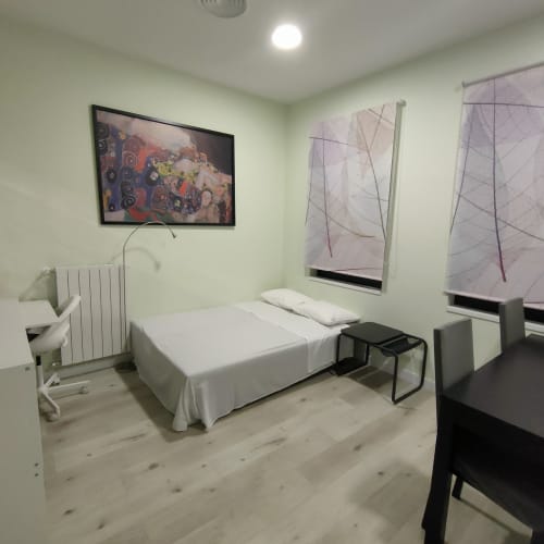 Dormitorio moderno en Megaleon apartment hotel de Segovia con cama blanca, radiador de calefacción y decoración minimalista