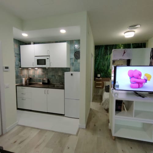 Cocina moderna y sala de estar en el apartamento Megaleon, Segovia, con muebles blancos y televisor de pantalla plana