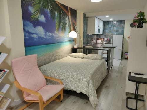Habitación del hotel Megaleon en Segovia con cama, mural temático de playa, cocina americana y sillón rosa