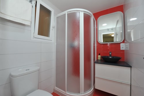 Baño moderno del hotel Megaleon en Segovia con pared de acento rojo, lavabo negro, cabina de ducha curva y accesorios blancos