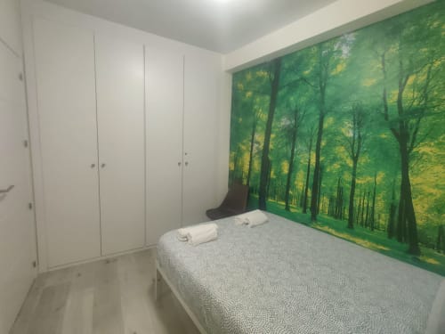 Habitación moderna del hotel Megaleon en Segovia con armario blanco, cama gris y mural de paisaje forestal.