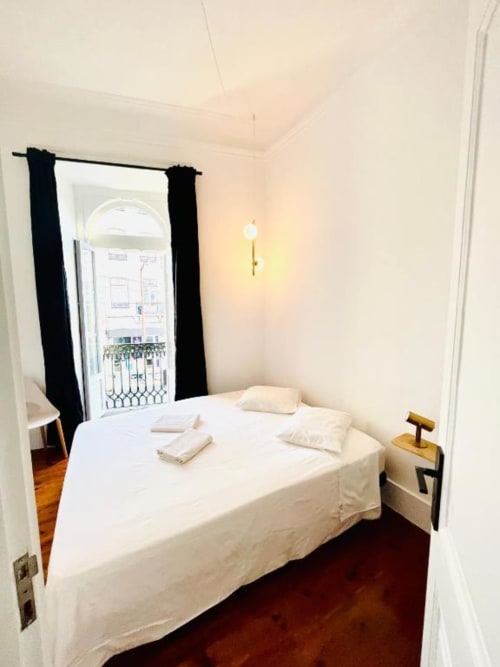 Bright bedroom at Royal Prince Garden Apartments in Lisboa with white bed, black curtains, balcony doors, and wooden floors