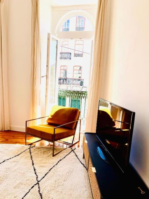 Modern living room at Royal Prince Garden Apartments in Lisbon with yellow armchair, flat-screen TV, and view of garden