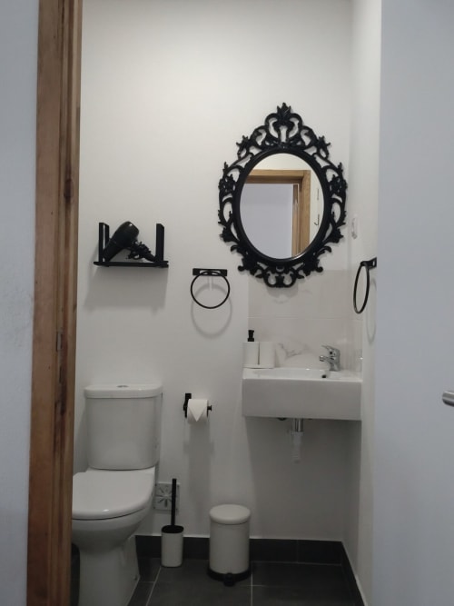 Banheiro moderno no apartamento Casa do Pão com pia branca, vaso sanitário, espelho preto ornamentado e acessórios em preto e branco.