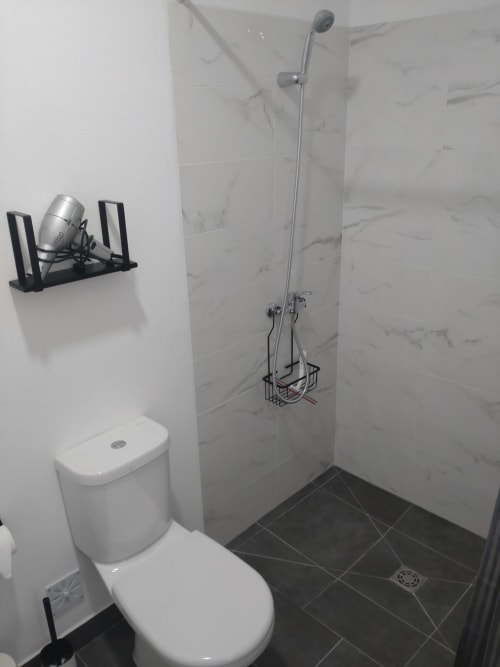 Modern bathroom with marble-tiled shower, white toilet, and black floor at Casa do Pão apartment in Campinho