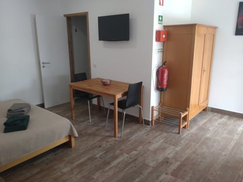 Spacious apartment room at Casa do Pão with wooden dining table, bed, wardrobe, TV, and emergency equipment in Campinho,