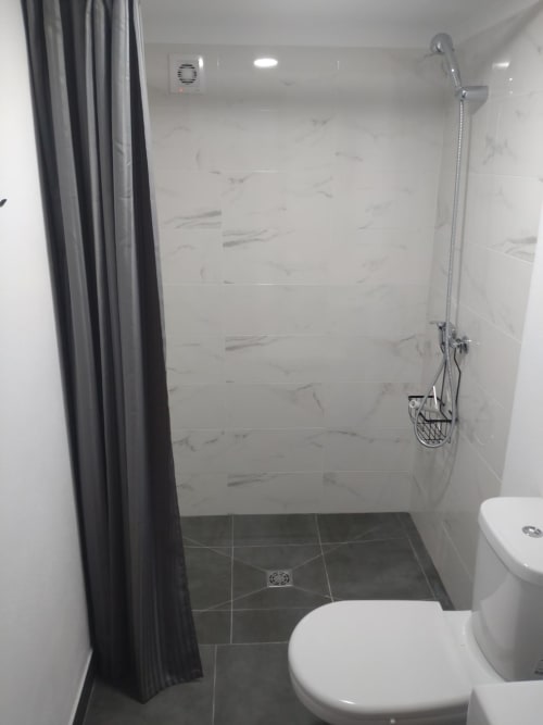Banheiro moderno com azulejos tipo mármore, piso escuro, chuveiro cabine com ducha manual, vaso branco, cortina cinza