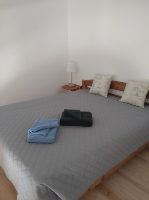 Quarto espaçoso na Casa do Pão com roupa de cama cinza, móveis de madeira, luminária e toalhas dobradas
