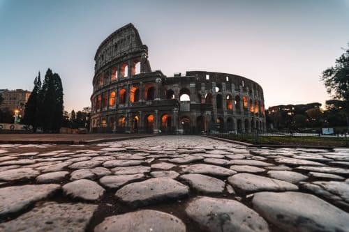 Colosseo romano antico illuminato al tramonto con piazza acciottolata, Hotel Zoelia, Roma