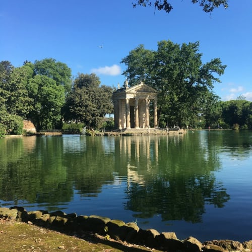 Padiglione tempio classico riflesso nelle acque tranquille di un lago circondato da lussureggiante vegetazione verde vicino a Roma