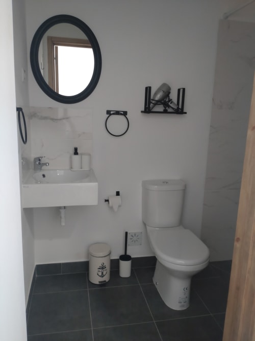Modern bathroom at Casa do Pão with circular mirror, white sink, toilet, and dark tile flooring