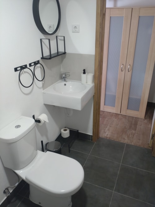 Banheiro moderno do apartamento Casa do Pão em Campinho com pia branca, vaso sanitário, azulejos escuros, espelho redondo e guarda-roupa de madeira