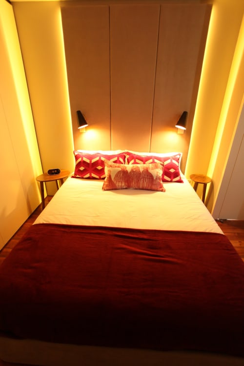Modern bedroom in Porto's New Oporto Apartments with ambient yellow lighting, white bedding, red decorative pillows, and