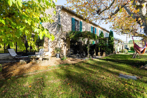 Cour de la maison d'hôtes Le Mas F à Saint-Rémy-de-Provence avec façade en pierre, volets verts, jardins luxuriants et espace détente