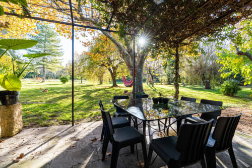 Espace de restauration extérieure au gîte Le Mas F à Saint-Rémy-de-Provence avec chaises noires et table ombragée sous les arbres