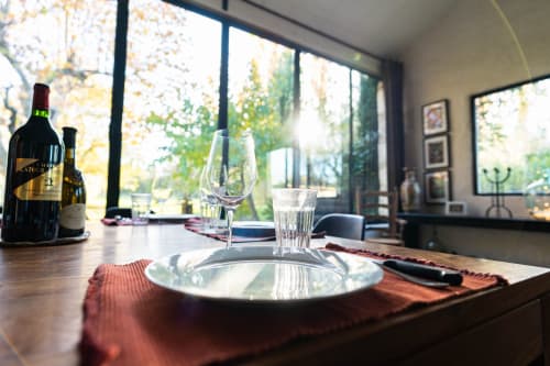 Élégante mise en place au Mas F à Saint-Rémy-de-Provence avec vin, couverts et vue sur le jardin par les grandes fenêtres
