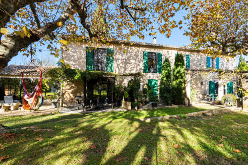 Cour du Mas F B&B à Saint-Rémy-de-Provence : maison en pierre, volets verts, feuillages d'automne et hamac.