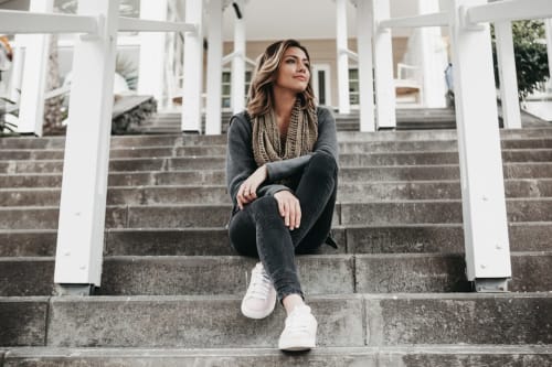 Mujer sentada en las escaleras de concreto del hotel LLUNA en Oaxaca, vistiendo ropa oscura y tenis blancos