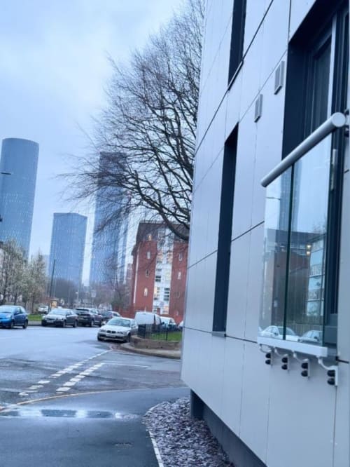 Modern apartment building in Manchester with contemporary architecture, parked cars, and city skyline view