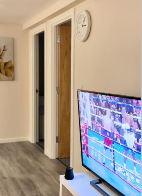 Modern apartment hallway at Cila Property Manchester with TV displaying stadium seating, wall clock, wooden doors, and