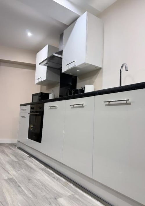Modern white kitchen with black countertop, built-in oven, cooktop, and upper storage cabinets in Manchester apartment