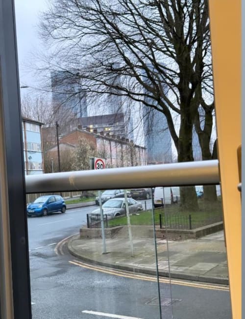 View from Cila Property apartment window in Manchester showing street, parked cars, bare trees, and 30km speed limit sign