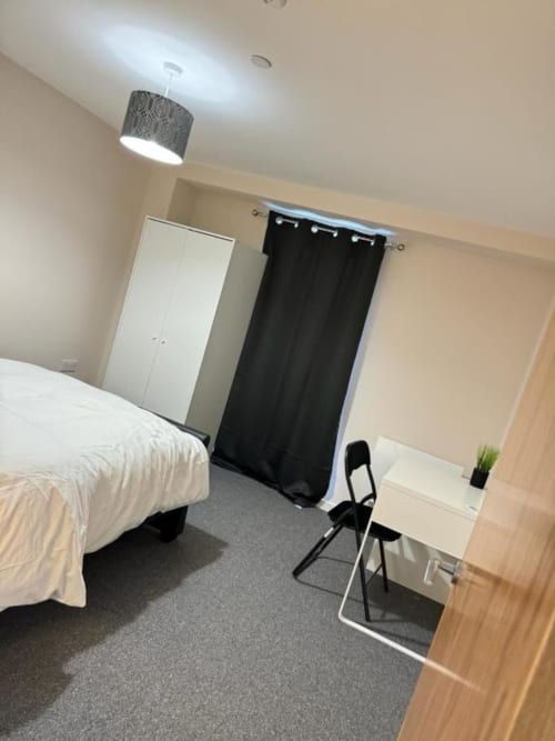 Modern bedroom at Cila Property Manchester apartment with white bed, black curtain, desk, chair, pendant light, and gray