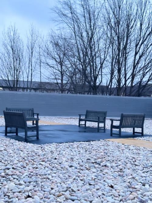Frozen lake view with bare trees and black Adirondack chairs on wooden deck and pebble beach at Cila Property Manchester