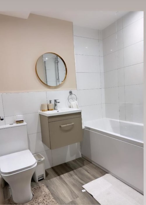 Modern bathroom at Cila Property Manchester apartment with white tiles, olive vanity, round mirror, bathtub, and wooden floor