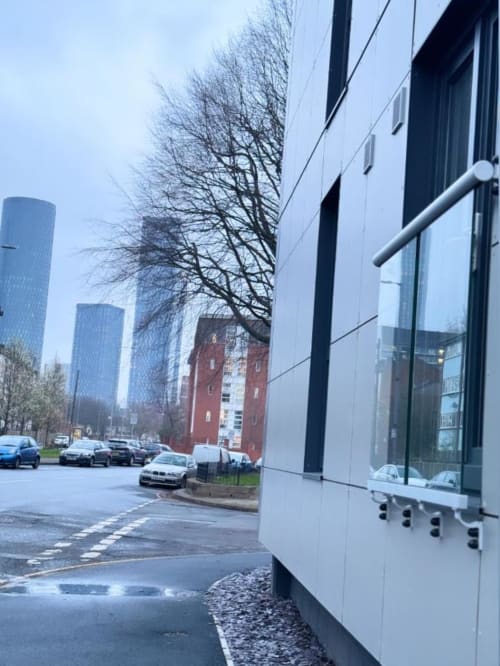Modern white building exterior at Cila Property Manchester with parked cars, bare tree, and glass windows overlooking city